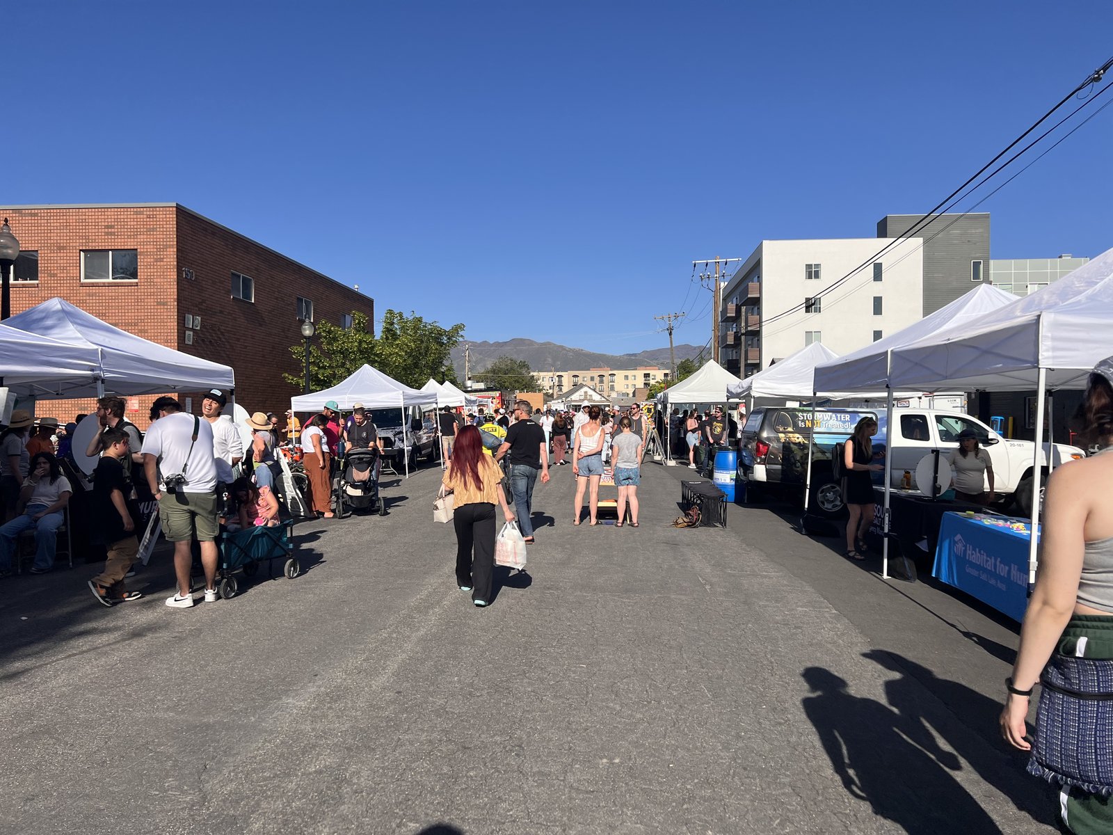 Wide view of Mural Fest with vendor tents lining the street and the Wasatch mountains in the distance